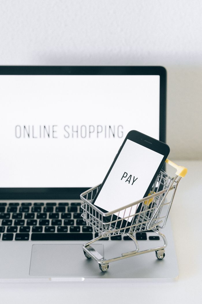 about-04 A smartphone in a miniature cart on a laptop symbolizes online shopping and digital payment.